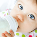 baby girl drinking from a glass baby bottle