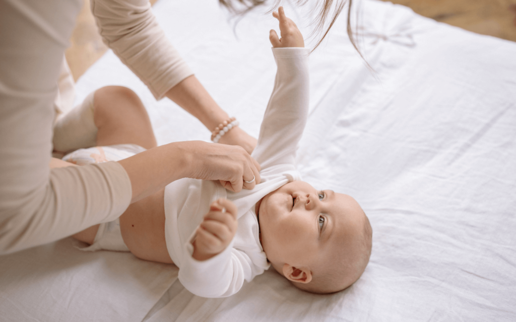 mom is dressung her baby with long-sleeved bodysuit