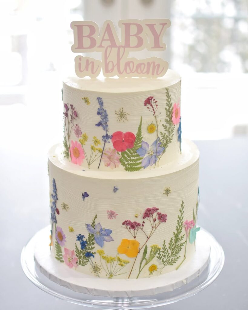 Two tier white cake decorated with dried flowers, with a sign that says Baby in Bloom