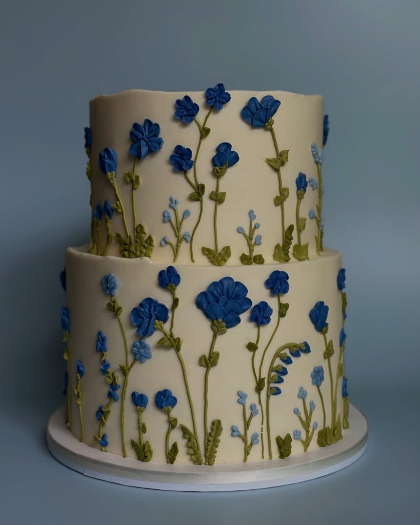 Two-tiered cake decorated with blue and green flower designs on a light blue background.