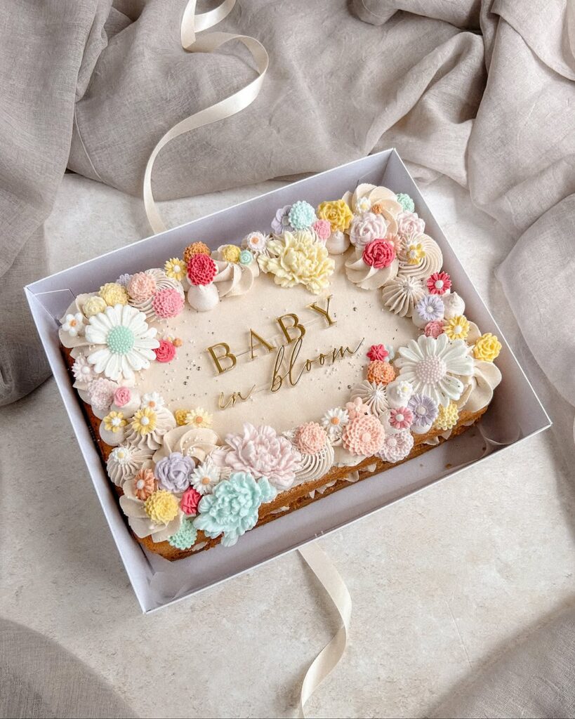 A decorated cake with pastel flowers and the words 'BABY in bloom' written in gold.