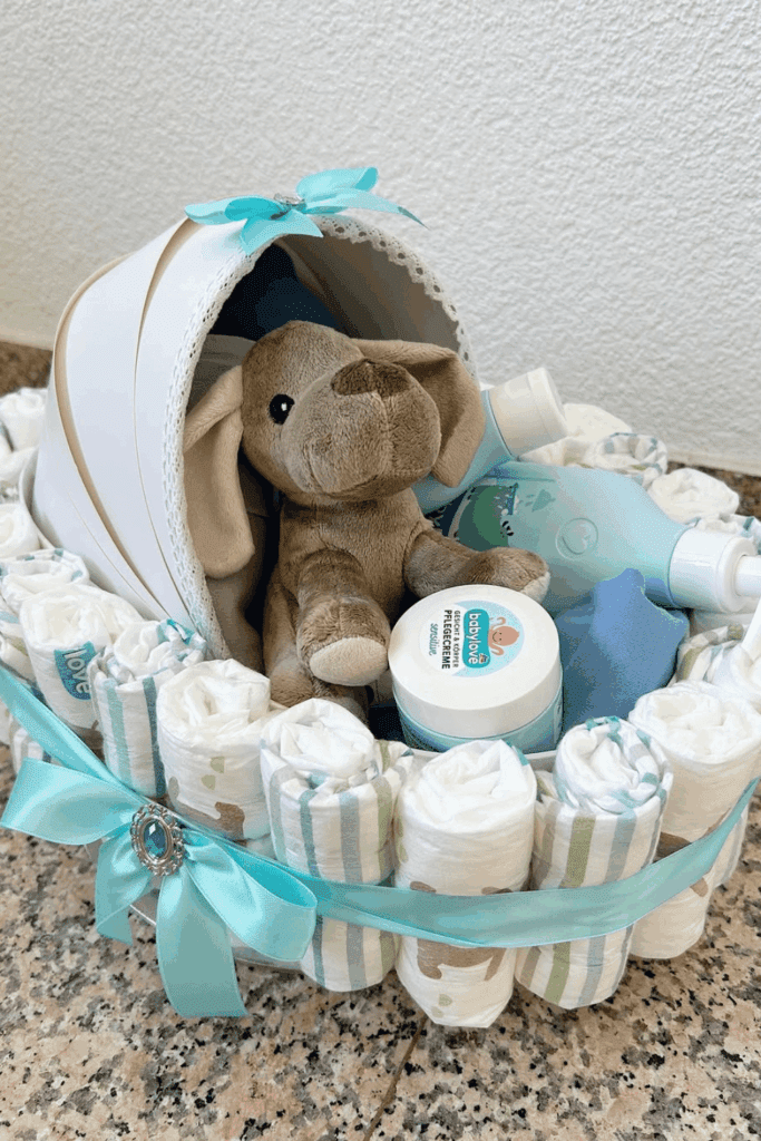 stroller-shaped diaper cake, adorned with light blue ribbons, a plush dog toy, and essential baby care items