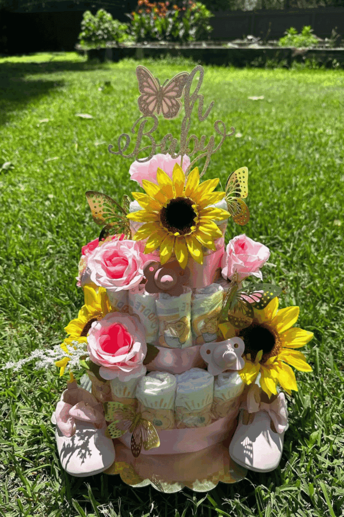 three-tiered diaper cake is adorned with vibrant sunflowers, delicate pink roses, and golden butterflies